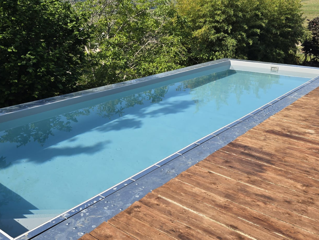 Piscina fuori terra Astrea in pannelli autoportanti con acqua azzurra bordo grigio e pedana in legno
