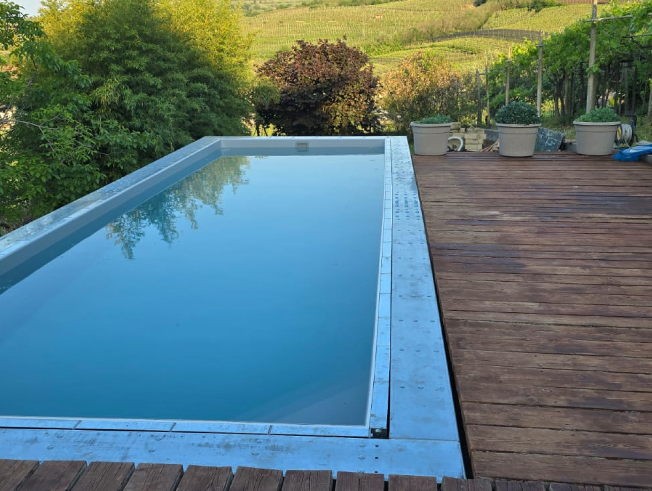 Piscina fuori terra rettangolare Astrea 8,65x3,05 m con deck in legno giardino e panorama collinare
